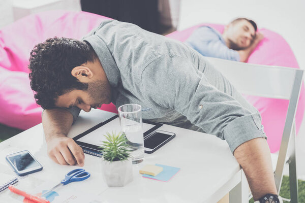 Молодые бизнесмены спят на столе и пуфы в современном офисе, бизнес-команда
