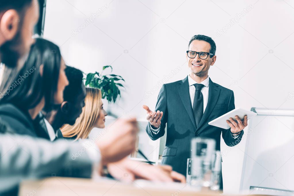 happy handsome team leader with tablet talking to multiracial managers in conference hall