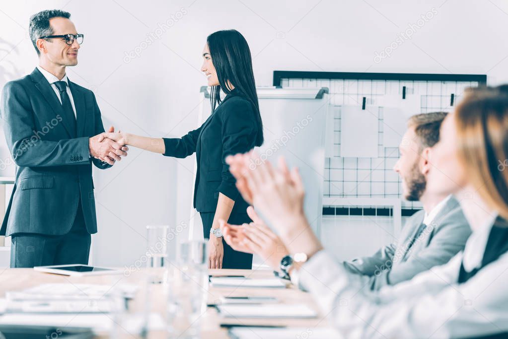 boss shaking hand of asian manageress at conference hall while colleagues clapping