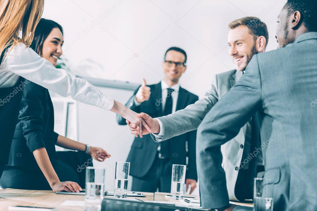 multicultural businesspeople shaking hands in conference hall while team leader showing thumb up