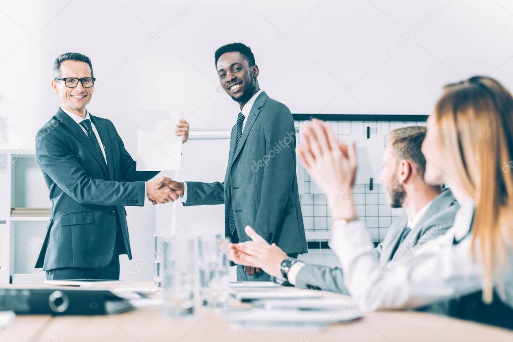 caucasian boss shaking hand of african american manager while colleagues clapping