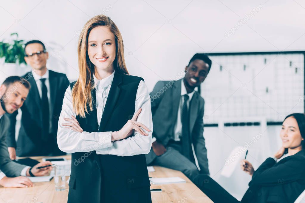 beautiful young businesswoman looking at camera with blurred multicultural colleagues on background