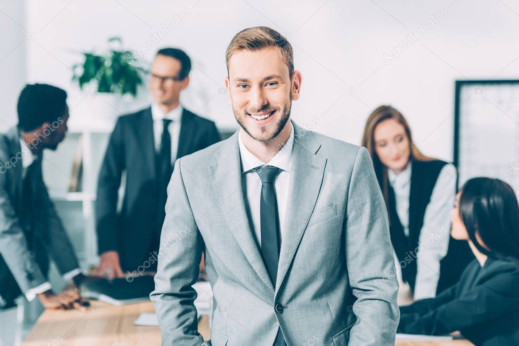 handsome young manager looking at camera with blurred multicultural businesspeople in conference hall