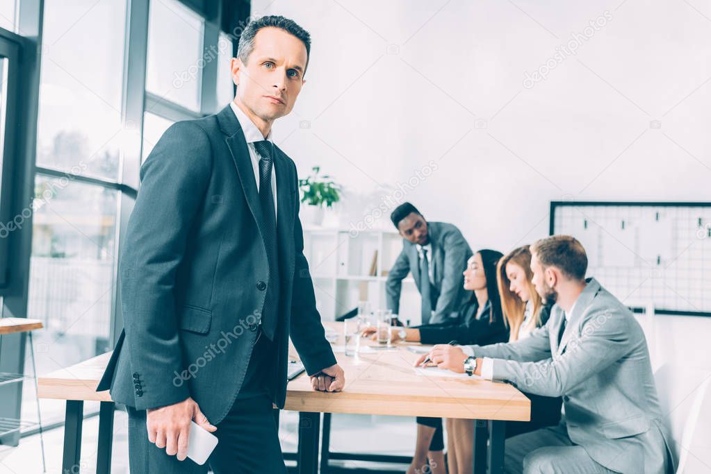 handsome businessman in suit standing in conference hall with multiracial colleagues having conversation