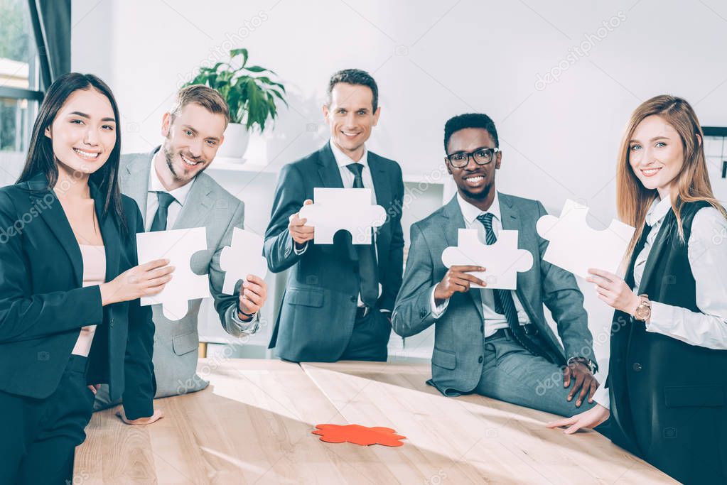 multiethnic businesspeople holding puzzle pieces together in conference hall