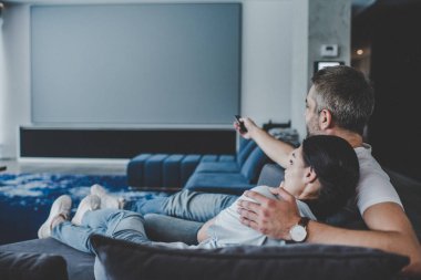 yetişkin adam kız arkadaşı kucaklayan ve evde kanepede televizyon izlerken uzaktan kumanda ile