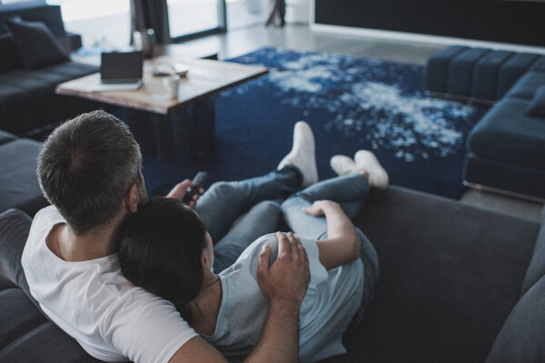 selective focus of adult man with remote controller embracing girlfriend and watching tv on sofa at home