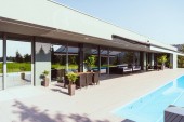 Modernes Ferienhaus mit Schwimmbad, kleinen Bäumen, Stühlen und Tischen 