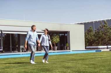 Çift el ele tutuşarak ve ülke evinde yeşil çim üzerinde birbirine bakarak güneş gözlüğü 