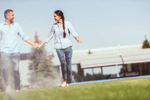 Feliz Pareja Cogida Mano Divertirse Con Riego Automático Hierba Cerca — Foto de stock gratis