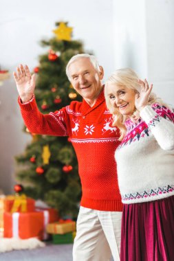 happy senior couple in christmas sweaters waving at camera clipart