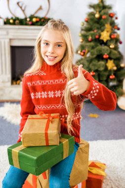 başparmak gösterilmesini yığılmış Noel hediye kutuları üzerinde oturan güzel mutlu çocuk