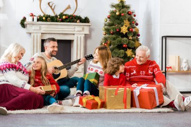 happy family sitting on floor together and listening guitar songs at home on christmas clipart