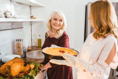 gülümseyen kıdemli anne ve kızı birlikte evde kabak pasta pişirme