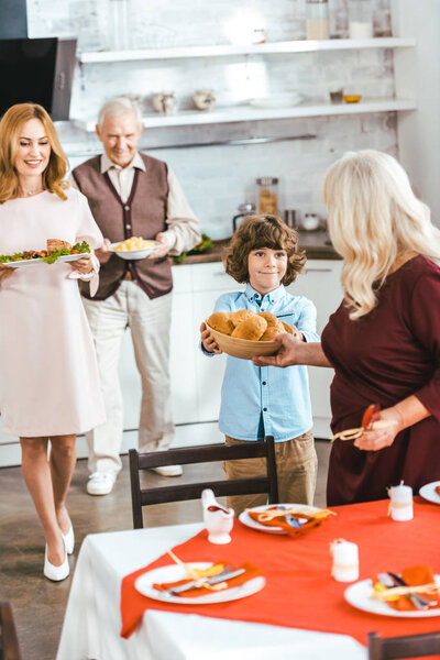 grandparents with daughter and little grandson serving table for thanksgiving dinner