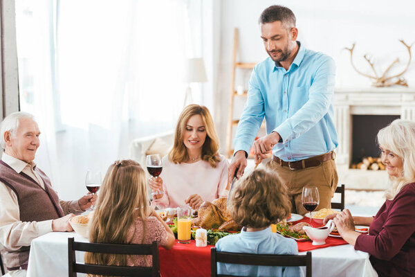happy family having delicious thanksgiving dinner together at home while father cutting turkey