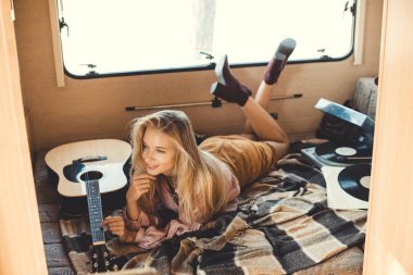 young woman lying inside campervan with acoustic guitar and vinyl player  clipart