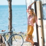 Atractiva chica hippie de pie cerca de autocaravana con bicicleta
