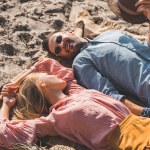 Hippie couple looking at each other and relaxing on blanket on sand