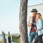 Young beautiful couple with glasses of red wine standing near trailer