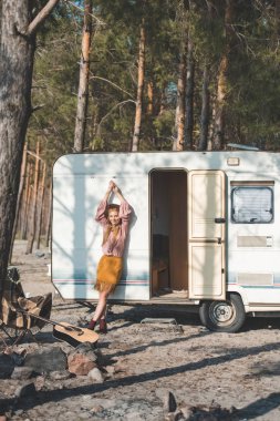 attractive hippie girl posing near campervan in forest clipart