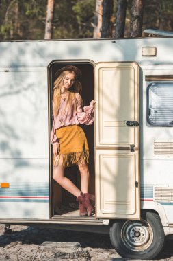 attractive hippie girl in hat posing in door of camper van clipart
