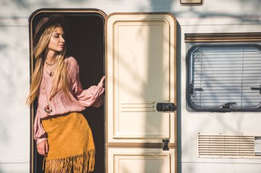 beautiful hippie girl in hat posing in door of trailer clipart