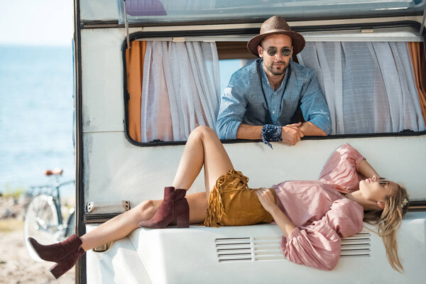 hippie girl lying on campervan with boyfriend near