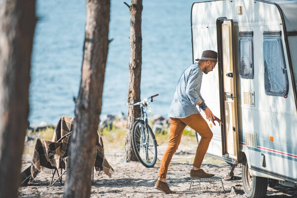young man going into trailer in camp with bicycle near the sea