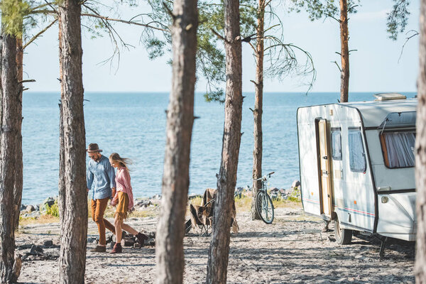 young couple holding hands and walking in nature near campervan