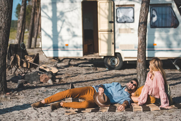 young happy couple relaxing on blanket near camper van