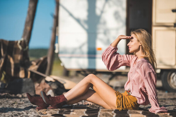 красивая молодая женщина смотрит в сторону и сидит на одеяле возле фургона Camper
