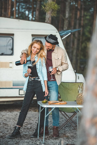 man pouring wine for girlfriend near trailer in camp