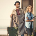 Handsome man wearing warm sweater on his girlfriend near trailer