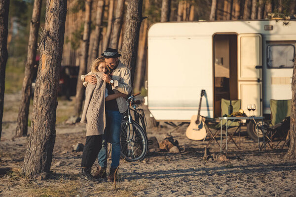 beautiful happy couple embracing in camp with trailer, bicycle and guitar