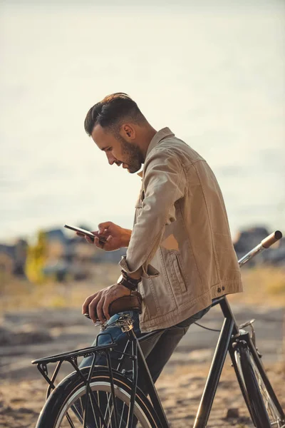 Όμορφος Νεαρός Χρησιμοποιώντας Smartphone Και Ακουμπά Στο Ποδήλατο Εξωτερικούς Χώρους — Φωτογραφία Αρχείου