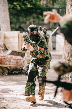 partial view of paintball player in uniform doing follow me gesture to his team outdoors clipart