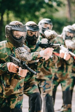 Koruyucu Maskeler ve kamuflaj paintball açık havada oyun ekibi ile işaret silah tutan kadın paintball oyuncu odaklı 