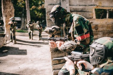 paintball marker silah ve açık havada ahşap duvar saklanıyor takım arkadaşı tutarak koruyucu maske Player'da seçici odak
