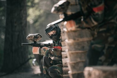paintball marker silah ve açık havada ahşap duvar saklanıyor takım arkadaşı tutarak koruyucu maske Player'da seçici odak