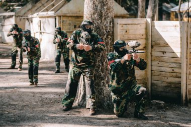 paintball oyuncu giyen kamuflaj ve işaretleri silah ağaç ve arka plan açık havada onların takım tarafından çekim maskeleri koruyucu gözlük