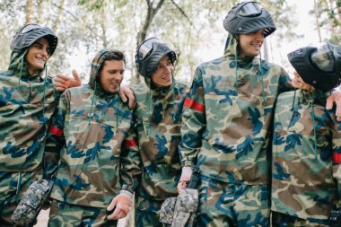 kamuflaj Paintball oyuncu konuşmak ve açık havada birbirlerine kucaklayan marker silahlarla gülümseyen 