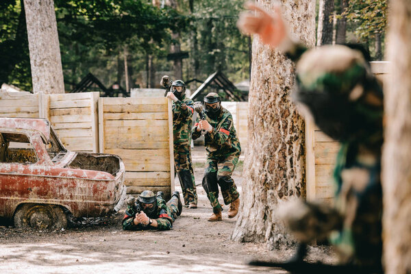 selective focus of paintball player doing follow me gesture to his paintball team in camouflage and masks outdoors 