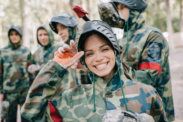 portrait of laughing female paintballer in uniform looking at camera while her team standing behind outdoors 
