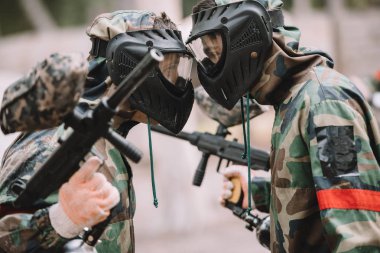 Koruyucu Maskeler ve kamuflaj yüz yüze açık havada duran erkek paintballers yan görünüm 