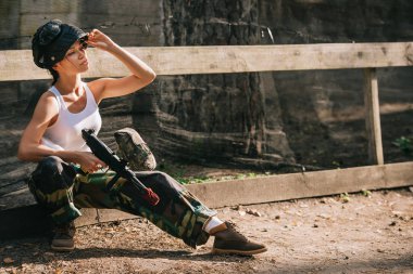 gözlüğü maske üzerine koyarak ve paintball silahı açık havada tutan beyaz singlet genç kadın paintballer