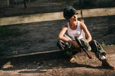 kendine güvenen genç kadın paintballer beyaz singlet ve paintball silahı açık havada tutan gözlüğü maskesi
