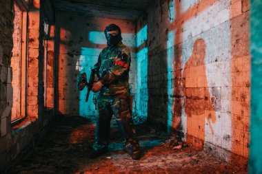 kendine güvenen erkek paintball oyuncu gözlüğü maskesi ve terk edilmiş binada paintball silahı tutan kamuflaj