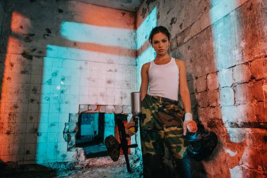 kamuflaj ve beyaz ciddi genç kadın paintballer singlet paintball silah tutup maske terk edilmiş binada koruyucu gözlük