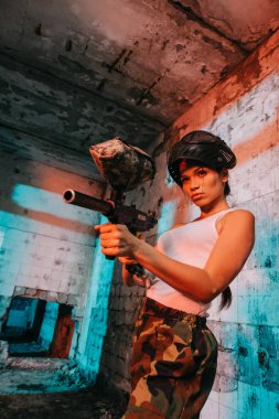 terk edilmiş binada paintball marker tarafından baş amaçlayan yukarıda gözlüğü maskesinde çekici genç kadın paintballer